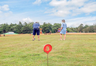 Dos personas juegan croquet en un campo verde de una casa de vacaciones en Pandrup, Dinamarca, con parque al fondo.