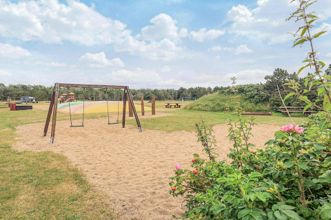 Parque infantil con columpios, zona de arena y mesas de picnic en Pandrup, Dinamarca, día soleado.
