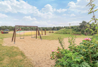 Parque infantil con columpios, zona de arena y mesas de picnic en Pandrup, Dinamarca, día soleado.