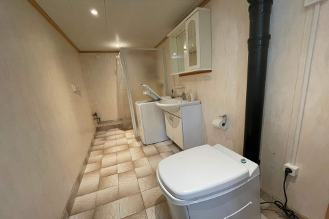 Baño largo con inodoro, lavadora, lavabo y ducha en el interior de una tranquila cabaña sueca.