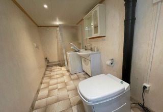 Langt badeværelse med toilet, vaskemaskine, håndvask og bruser i en svensk fredelig bjælkehytte.