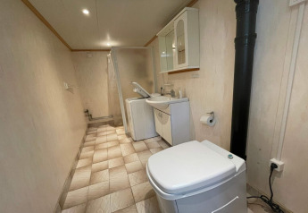 Baño largo con inodoro, lavadora, lavabo y ducha en el interior de una tranquila cabaña sueca.