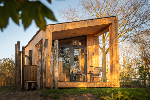 Wellness Duynzicht lodge with wooden exterior, large windows, outdoor seating, and lush trees in sunlight.