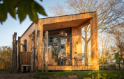 Moderne Wellness Duynzicht Lodge aus Holz mit großen Fenstern, Terrasse und Natur im Sonnenlicht.