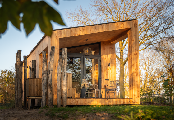 Wellness Duynzicht lodge with wooden exterior, large windows, outdoor seating, and lush trees in sunlight.