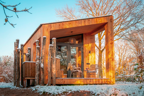 Modernes Holzhaus Wellness Duynzicht bei Sandberghe, Niederlande, umgeben von verschneiten Bäumen.