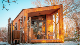 Modernes Holzhaus Wellness Duynzicht bei Sandberghe, Niederlande, umgeben von verschneiten Bäumen.