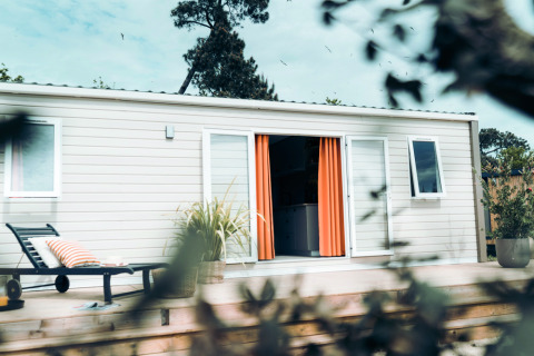 Moderne lodge met oranje gordijnen en ligzetel op houten terras bij Eurocamping Vessem BV in Nederland.