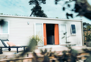 Moderne lodge met oranje gordijnen en ligzetel op houten terras bij Eurocamping Vessem BV in Nederland.