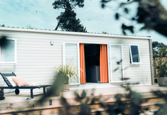 Moderne lodge met oranje gordijnen en loungebank op houten terras bij Eurocamping Vessem BV in Nederland.