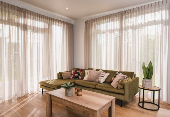 Moderne leefruimte in een luxelodge bij Vakantiepark Hölte, Nederland, met groene zetel, planten en raam.