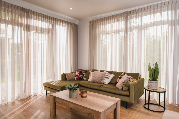 Wohnzimmer einer Luxuslodge im Vakantiepark Hölte, Niederlande, mit grüner Couch, Pflanzen und Fensterfront.