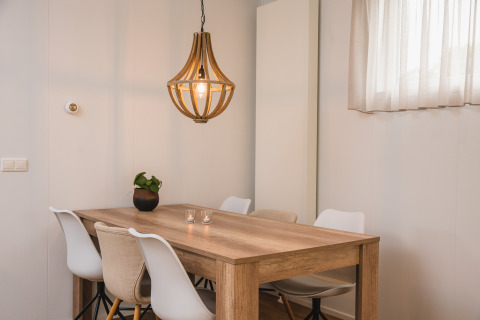 Zona pranzo moderna con tavolo in legno, sedie bianche e lampada a sospensione presso Luxury lodge a Vakantiepark Hölte, Paesi Bassi.