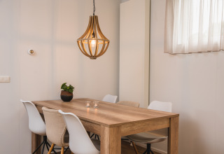 Comedor moderno con mesa de madera, sillas blancas y lámpara colgante en Luxury lodge de Vakantiepark Hölte, Países Bajos.