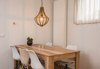Zona pranzo moderna con tavolo in legno, sedie bianche e lampada a sospensione presso Luxury lodge a Vakantiepark Hölte, Paesi Bassi.