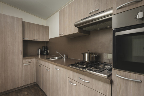 Moderne keuken met lichte houten kasten, gasfornuis en oven in Cosy cabin bij Vakantiepark Hölte.