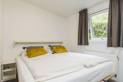 Acogedor dormitorio en una cabaña de Vakantiepark Hölte, Países Bajos, con cama grande y ventana luminosa.