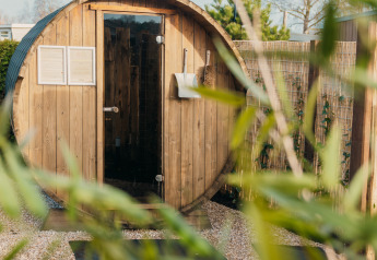 Sauna en forme de tonneau à l'extérieur de Veluwe lounge + sauna, Holiday park De Boshoek, Pays-Bas, entouré de plantes.