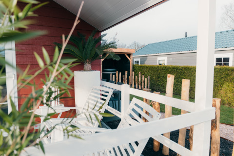 Veranda met witte stoelen en groene planten aan Veluwe lounge + sauna in vakantiedomein De Boshoek, Nederland.