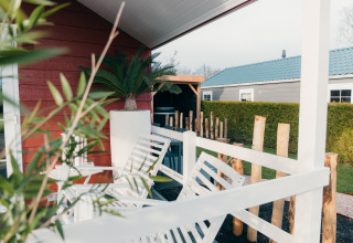 Veranda mit weißen Stühlen und grünen Pflanzen, Veluwe Lounge + Sauna im Ferienpark De Boshoek, Niederlande.