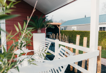Veranda mit weißen Stühlen und grünen Pflanzen, Veluwe Lounge + Sauna im Ferienpark De Boshoek, Niederlande.