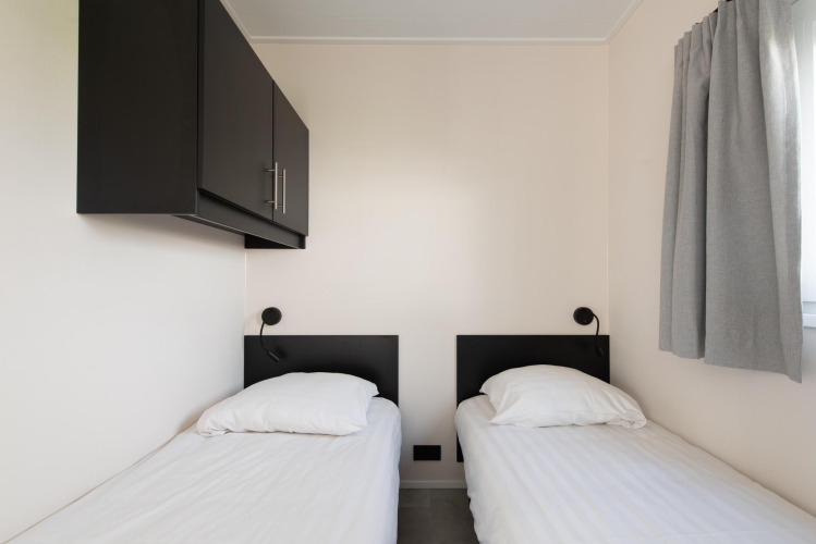 Deux lits simples avec draps blancs dans une chambre moderne de la Wood Lodge avec climatisation à Kompas Camping Nieuwpoort.