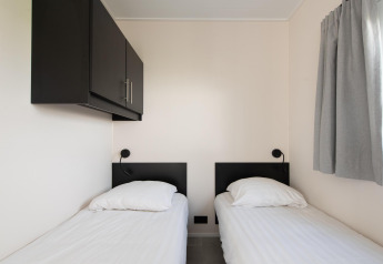 Deux lits simples avec draps blancs dans une chambre moderne de la Wood Lodge avec climatisation à Kompas Camping Nieuwpoort.