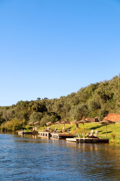Houten steigers met loungestoelen en parasols aan het meer bij Dome House Duplex Do Lago, Wecamp Reserva Alecrim, Portugal.