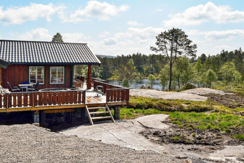 Udendørsbillede af 76409 TROLLHYTTA lodge med terrasse og skovklædt sølandskab i baggrunden.
