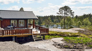 Vista exterior del lodge 76409 TROLLHYTTA con terraza de madera y paisaje de lago y bosque al fondo.