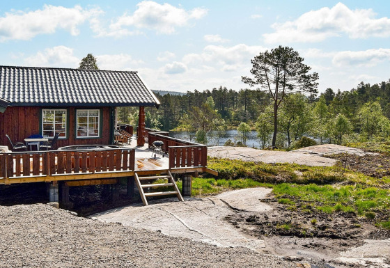 Udendørsbillede af 76409 TROLLHYTTA lodge med terrasse og skovklædt sølandskab i baggrunden.