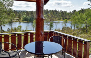 Vue depuis la terrasse en bois du lodge 76409 TROLLHYTTA au Danemark, lac, forêt et chaises en extérieur.