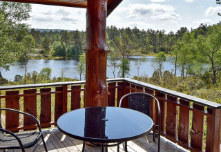 Udsigt fra træterrasse på 76409 TROLLHYTTA lodge i Danmark med sø, skov og havemøbler i forgrunden.