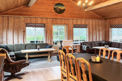 Hyggelig stue i Trollhytta-lodgen, Danmark, med trægulv, pejse, sofaer og store vinduer med udsigt.