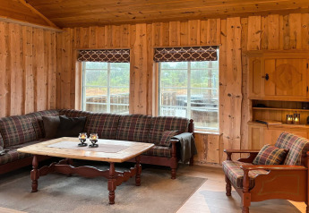 Salon chaleureux de lodge en bois avec canapé à carreaux, table en bois et grandes fenêtres à Trollhytta, Danemark.
