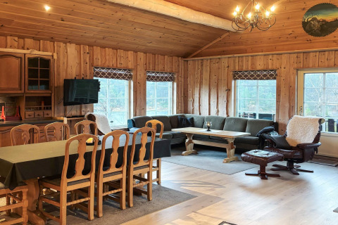 Stort opholdsrum i lodge 76409 TROLLHYTTA i Danmark med træpaneler, spisebord, sofa og pejsestol.
