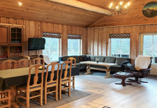 Stort opholdsrum i lodge 76409 TROLLHYTTA i Danmark med træpaneler, spisebord, sofa og pejsestol.