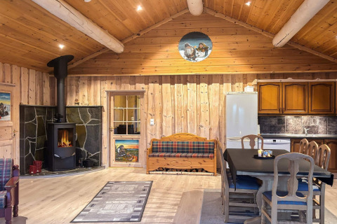 Hyggelig stue i TROLLHYTTA lodge, Danmark, med træinteriør, brændeovn og spiseplads ved køkkenet.