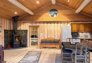 Hyggelig stue i TROLLHYTTA lodge, Danmark, med træinteriør, brændeovn og spiseplads ved køkkenet.