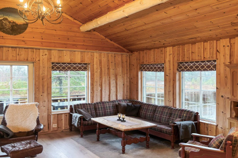 Stue i TROLLHYTTA-lodge i Danmark med trævægge, plaidmøbler og store vinduer med udsigt til naturen.
