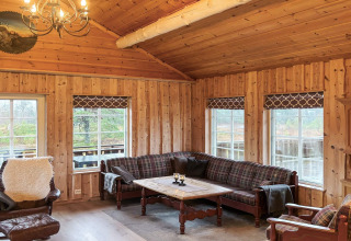 Stue i TROLLHYTTA-lodge i Danmark med trævægge, plaidmøbler og store vinduer med udsigt til naturen.