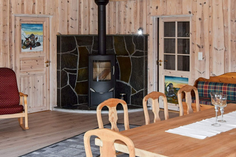 Stue i Trollhytta lodge i Danmark med træpaneler, brændeovn, spisebord og farverigt interiør.