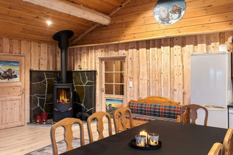 Hyggelig stue i Trollhytta med brændeovn, træinteriør, spisebord, plaid-sofa og stearinlys.