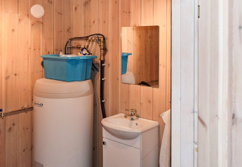 Salle de bain en bois avec chauffe-eau, boîte de rangement bleue sur le dessus et petit lavabo avec miroir.
