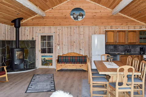 Indretning af en hyggelig hytte i træ med brændeovn, spisebord, køkken og sofa på Trollhytta i Danmark.