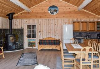 Indretning af en hyggelig hytte i træ med brændeovn, spisebord, køkken og sofa på Trollhytta i Danmark.