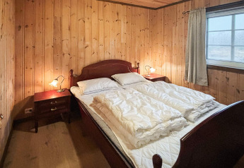 Chambre du lodge 76409 TROLLHYTTA au Danemark avec murs boisés, grand lit et fenêtre lumineuse.