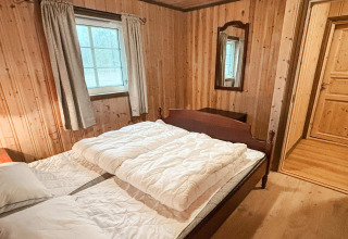 Soveværelse i lodge '76409 TROLLHYTTA' i Danmark med trævægge, dobbeltseng og vindue.