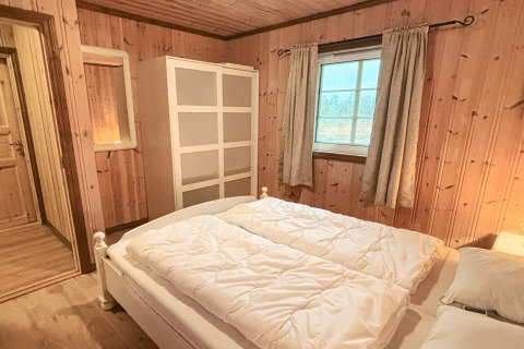 Soveværelse i TROLLHYTTA-lodge i Danmark med trævægge, dobbeltseng, garderobe og vindue.