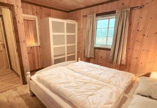 Soveværelse i TROLLHYTTA-lodge i Danmark med trævægge, dobbeltseng, garderobe og vindue.